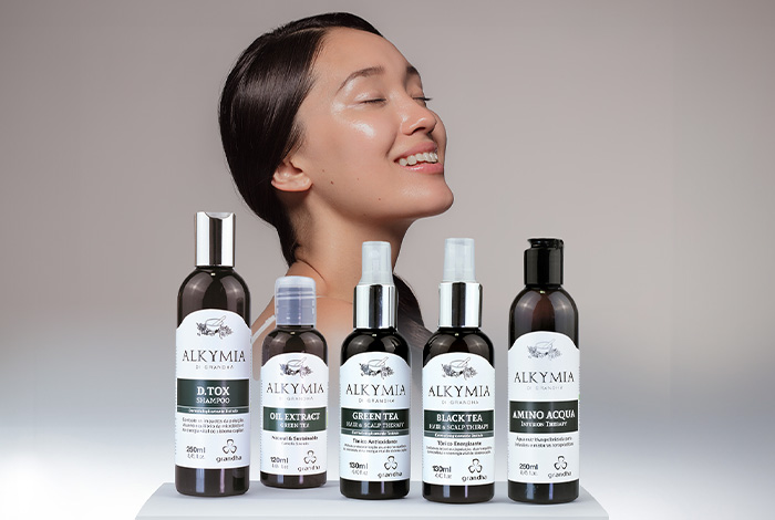 Linha de produtos Alkymia exibida em destaque com uma mulher de pele luminosa ao fundo, simbolizando cuidados naturais para pele e cabelo.