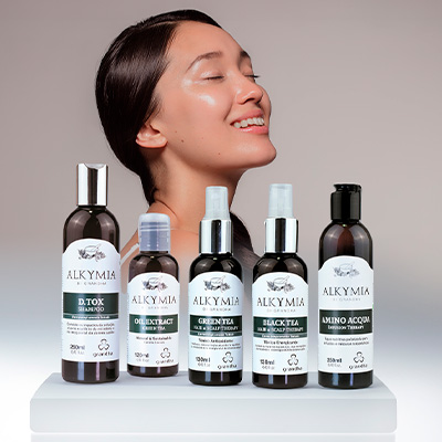 Linha de produtos Alkymia exibida em destaque com uma mulher de pele luminosa ao fundo, simbolizando cuidados naturais para pele e cabelo.