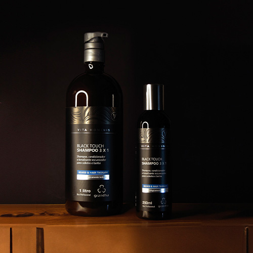 Dois frascos do Shampoo Black Touch 3x1 da Grandha, posicionados sobre uma superfície de madeira, destacados por um fundo preto minimalista.