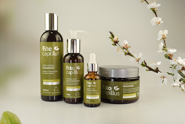 Linha de produtos Fito Capillus da Grandha para terapia capilar, exibindo shampoo, sérum e máscara ao lado de galhos floridos em fundo neutro.