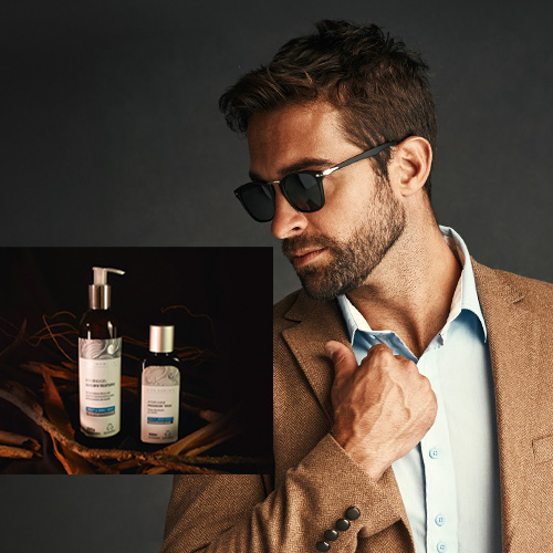 Homem estiloso de barba e óculos escuros ajustando o paletó, com destaque para produtos de cuidados masculinos ao fundo, sugerindo sofisticação.